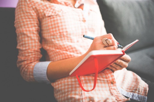 Person writing in red notebook